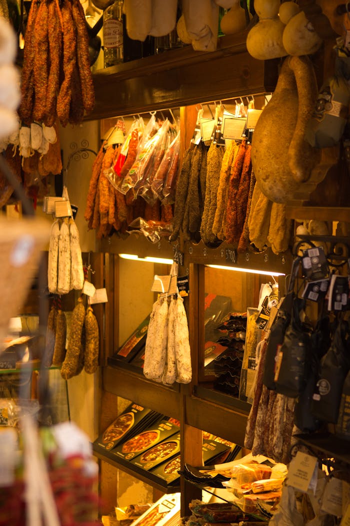 services-02 Cured meats hanging on shelves in a rustic gourmet food shop, warm ambiance.