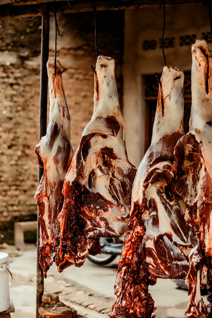 services-03 Close-up of butchered animal carcasses hanging in an outdoor market setting.